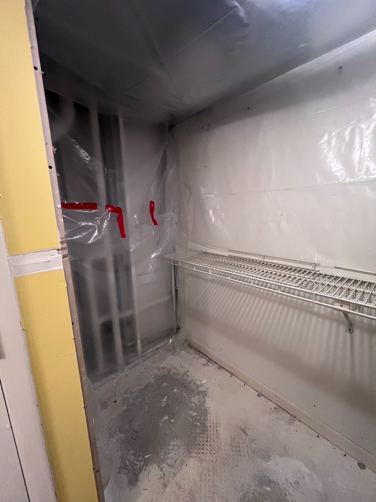 Wide view of the closet interior with plastic containment sheeting installed along the walls and ceiling