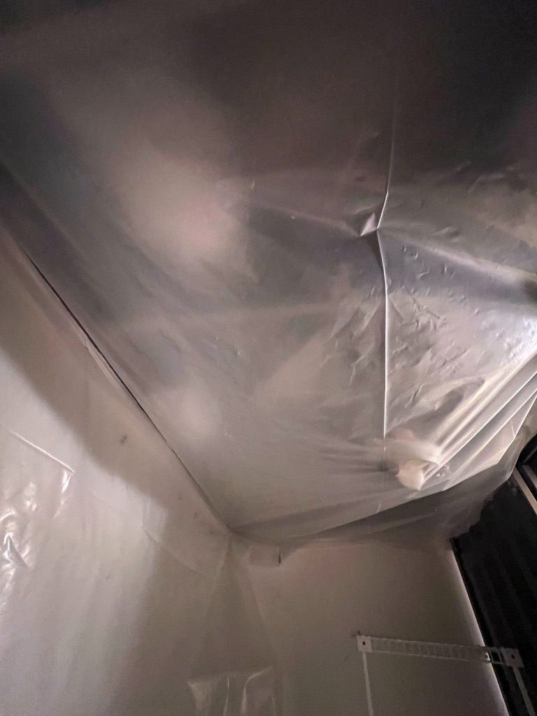 Close-up of ceiling containment sheeting at the corner of the affected closet
