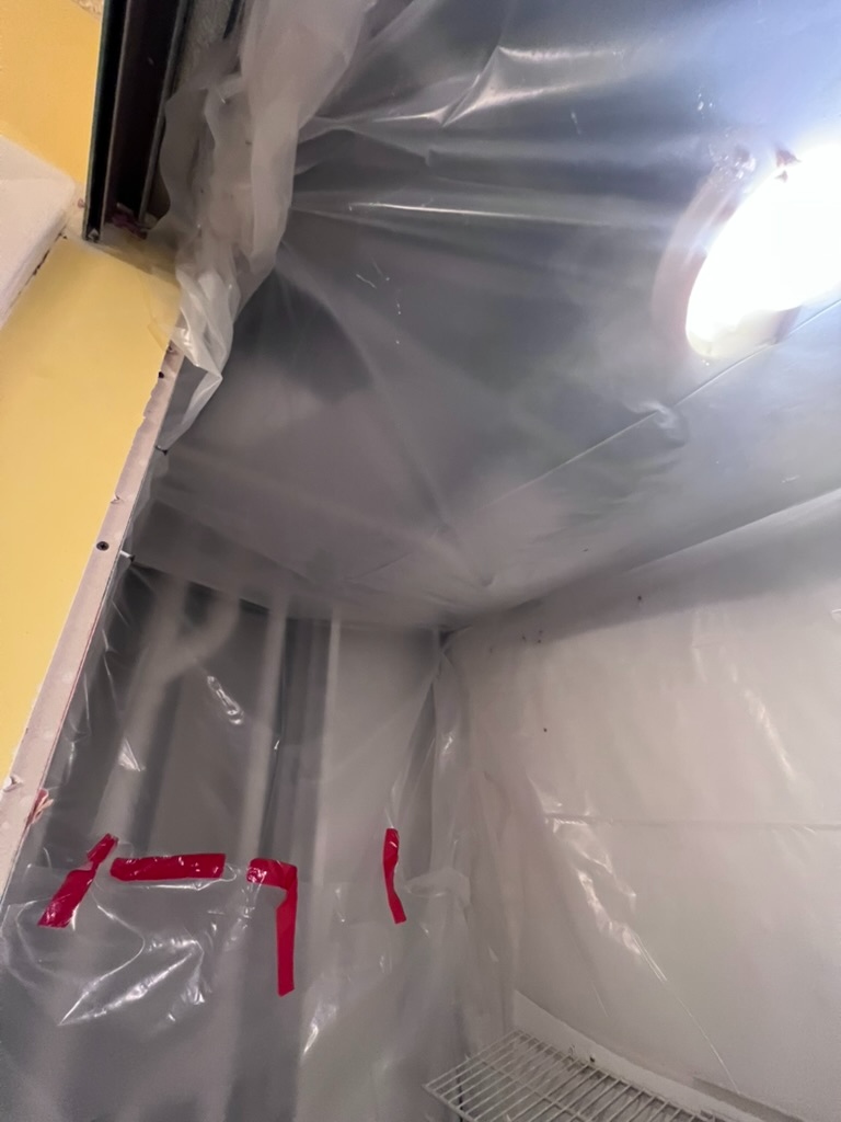 Detailed view of red tape sealing containment sheeting seams inside the previously affected closet