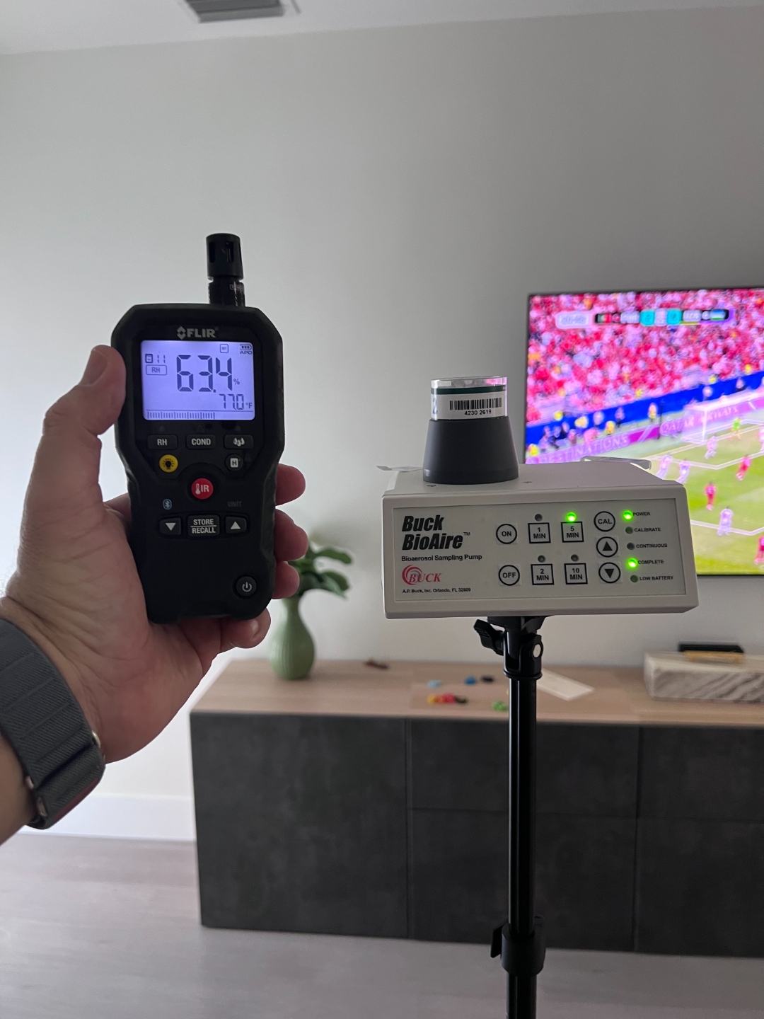 Buck BioAire bioaerosol sampling pump collecting an indoor air quality sample alongside a FLIR moisture meter reading