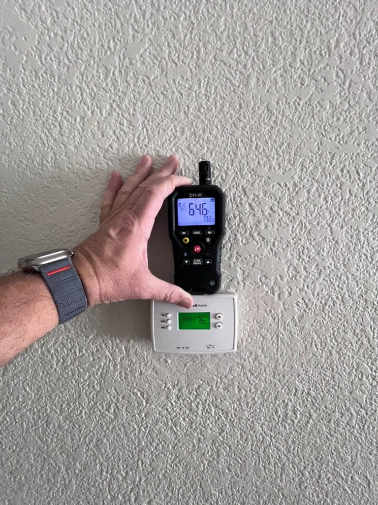 Inspector taking a moisture meter reading on an interior wall surface during a field inspection