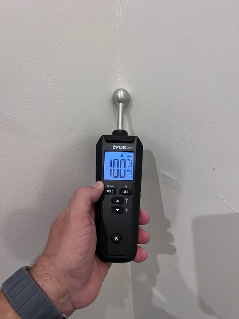 Moisture meter reading on a saturated interior wall showing elevated moisture content