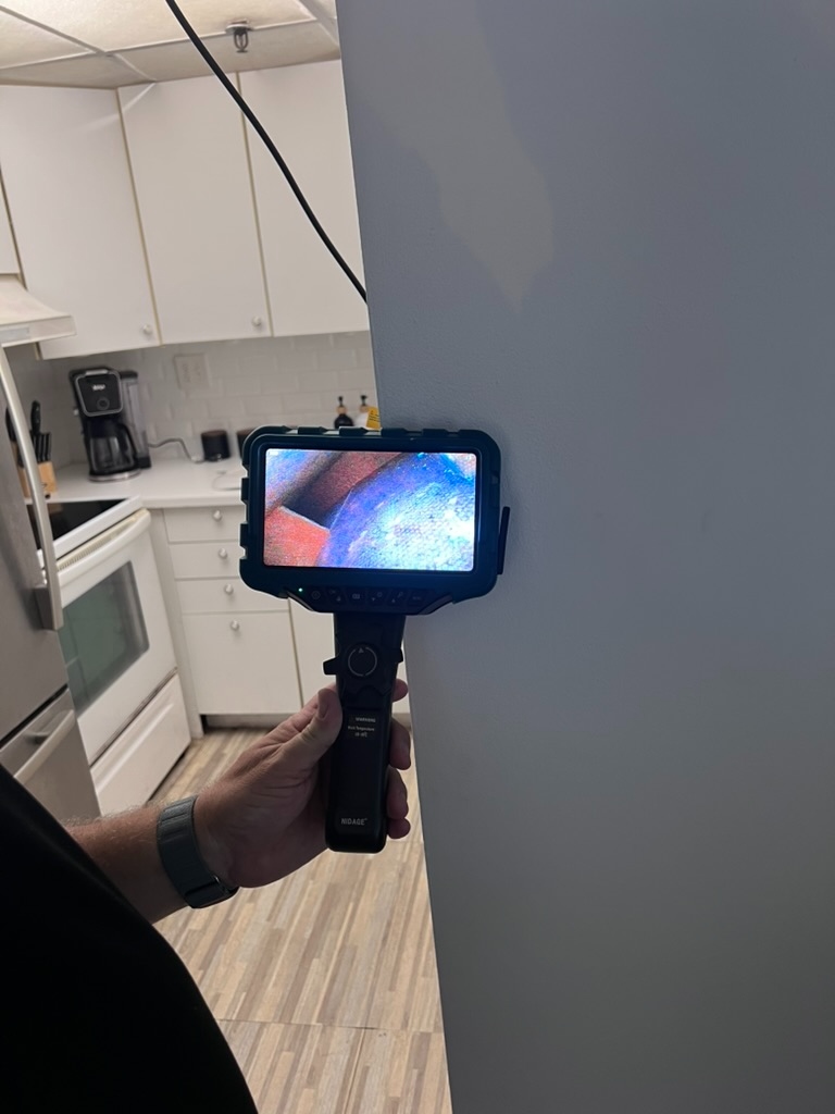 Video borescope camera inserted into a wall opening showing a live feed on the handheld monitor
